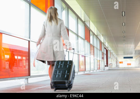 Full length rear view of young businesswoman with luggage rushing in railroad station Stock Photo