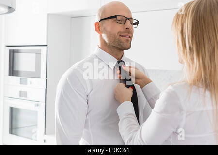 Woman adjusting businessman's tie at home