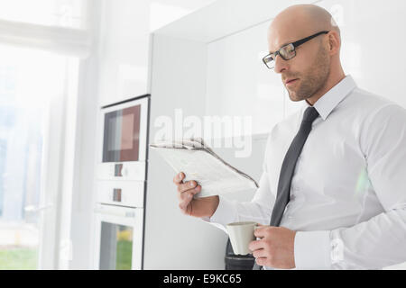 Mid adult businessman having coffee while reading newspaper at home Stock Photo