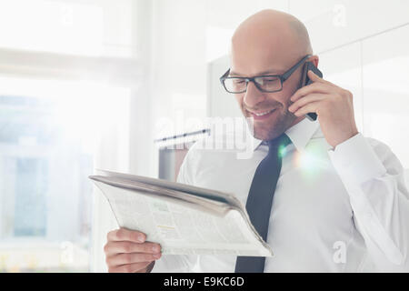 Happy businessman on call while reading newspaper at home Stock Photo