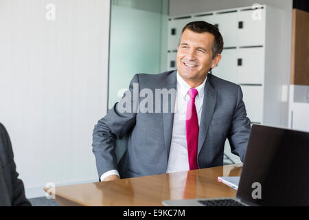 Happy mature businessman sitting at desk in office Stock Photo