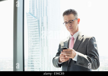 Mature businessman using cell phone by window Stock Photo
