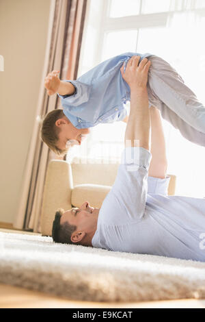 Side view of playful father picking up son while lying on floor at home Stock Photo