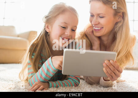 Happy mother and daughter using digital tablet on floor at home Stock Photo
