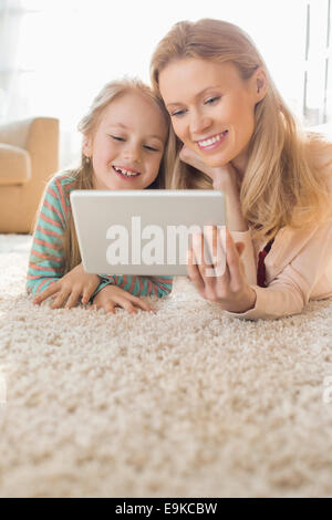 Happy mother and daughter using digital tablet on floor at home Stock Photo