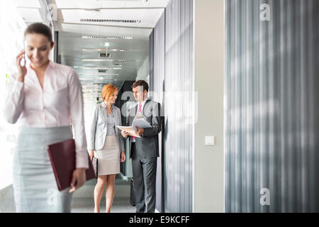 Business people discussing in corridor with colleague using cell phone in foreground Stock Photo
