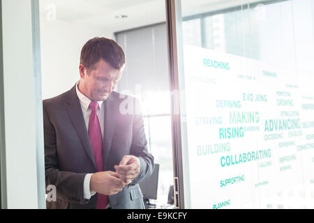 Mature businessman buttoning sleeve in office Stock Photo