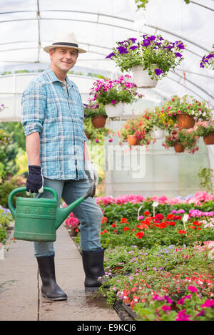 Full-length portrait of smiling man carrying watering can in greenhouse Stock Photo