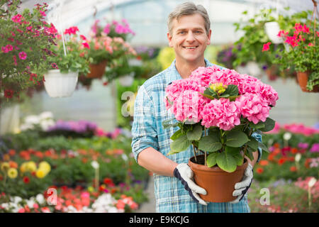 Portrait of happy gardener holding flower pot in greenhouse Stock Photo