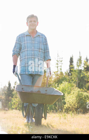 Portrait of male gardener pushing wheelbarrow at garden Stock Photo