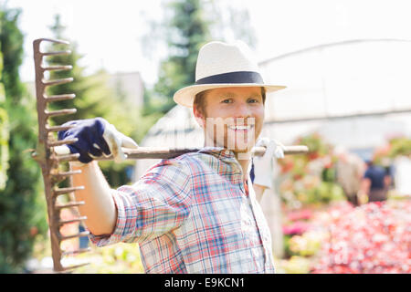 Portrait of smiling gardener carrying rake on shoulders at plant nursery Stock Photo