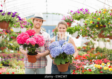 Portrait of smiling gardeners holding flower pots at greenhouse Stock Photo