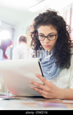 Young businesswoman reading notepad at creative office with colleagues in background Stock Photo