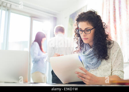 Businesswoman reading notepad at creative office with colleagues in background Stock Photo
