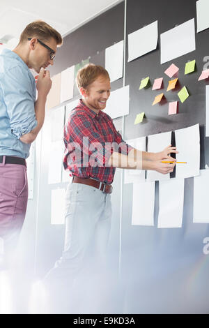 Creative businessmen discussing over document on wall in office Stock Photo