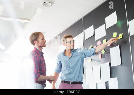 Creative businessmen discussing over sticky paper on wall in office Stock Photo