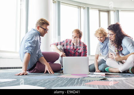 Businesspeople using laptop while sitting on floor at creative office Stock Photo
