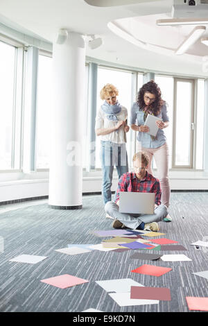 Businesswomen looking at male colleague using laptop on floor in creative office Stock Photo