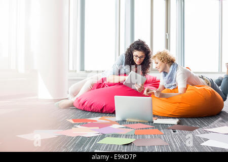 Creative businesswomen using tablet PC while relaxing on beanbag chairs at office Stock Photo