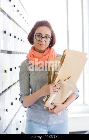 Portrait of confident businesswoman holding envelopes in locker room at creative office Stock Photo