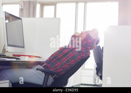 Side view of young businessman relaxing at computer desk in office Stock Photo