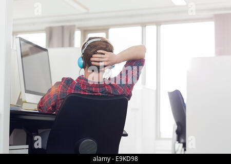 Rear view of young businessman wearing headphones at computer desk in office Stock Photo