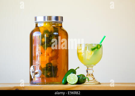 Tequila infused with jalapeno peppers in a tea jar at a restaurant bar. Stock Photo