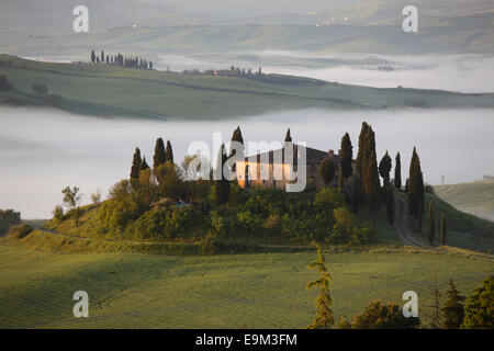 The Belvedere farmhouse in Val d’Orcia with early morning fog, San Quirico d'Orcia, Tuscany, Italy Stock Photo
