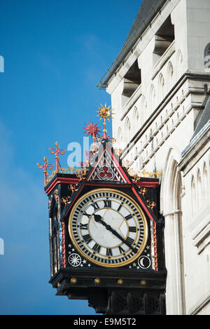 Royal Courts of Justice Victorian Clock London Close Up | LONDON, United Kingdom — The Victorian bracket clock of the Royal Courts of Justice on the Strand displays its full ornamental face — Roman numerals on a white dial, a gilded bezel, and a Gothic canopy crowned with a sunburst finial — against the building's Portland stone Gothic Revival facade. Designed by George Edmund Street and completed in 1882, the courthouse stands at the historic boundary between the City of London and the City of Westminster, and the clock's prominent position signals that boundary to this day. Stock Photo