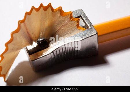 Macro close-up of a classic metal pencil sharpener shaving a traditional yellow wooden pencil,producing a textured wooden shaving on white background. Stock Photo