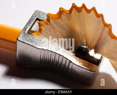 Macro close-up of a classic metal pencil sharpener shaving a traditional yellow wooden pencil,producing a textured wooden shaving on white background. Stock Photo