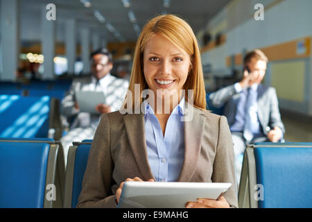 Smiling young woman with touchpad looking at camera while sitting in airport Stock Photo