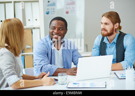 Two male employees listening to explanations of their colleague at business meeting
