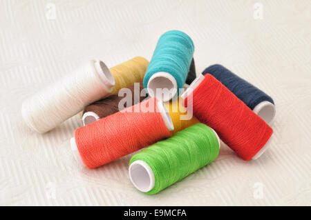 Sewing threads of different colors on white tablecloth closeup image Stock Photo