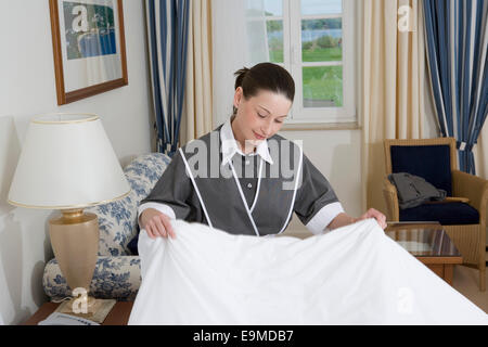 Uniformed maid making bed in hotel room Stock Photo