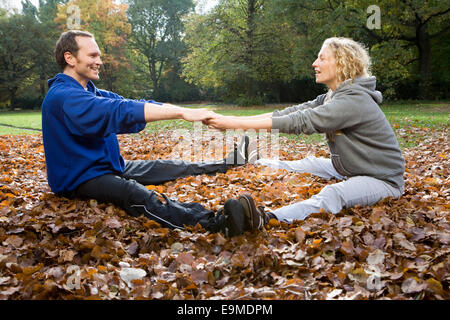Man and woman sitting and stretching on autumn leaves in park Stock Photo