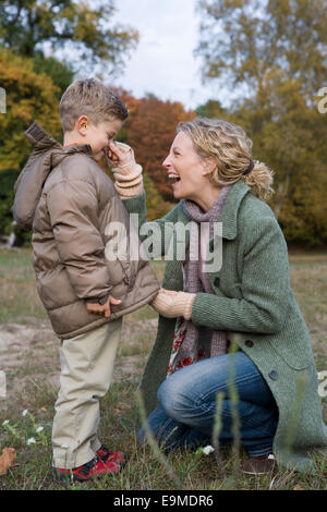 Mother pinching son’s nose in park whilst zipper up parka Stock Photo
