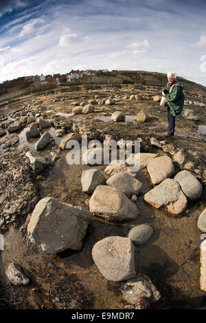 UK, England, Yorkshire, Robin Hood’s Bay, visitor looking in rock pools, fish-eye wide angle lens view