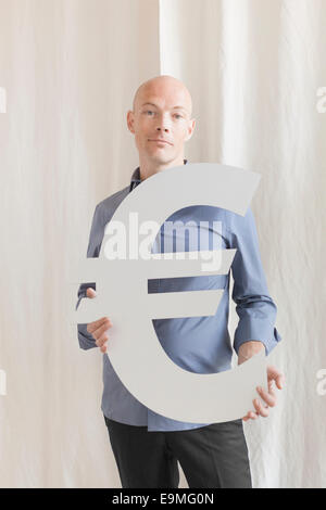 Portrait of confident businessman holding euro symbol at office Stock Photo