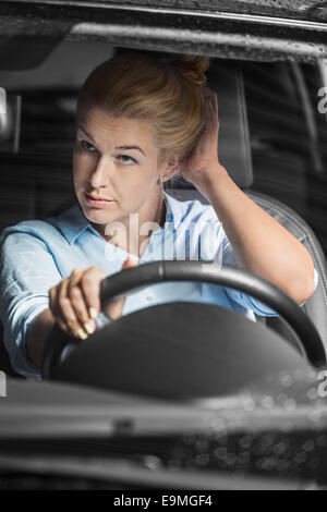 Mid adult woman looking at herself in rear-view mirror while driving car Stock Photo