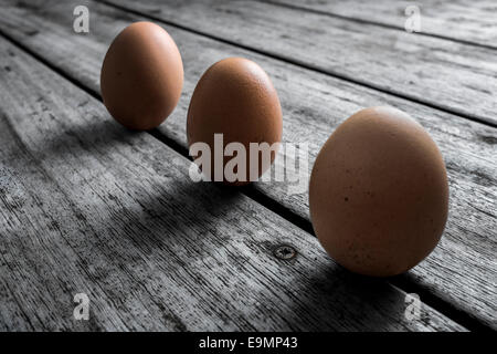 Three free range chicken eggs arranged on a desaturated wooden background. Stock Photo