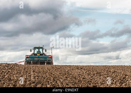 tractor seeding in a field on cloudy sky background Stock Photo