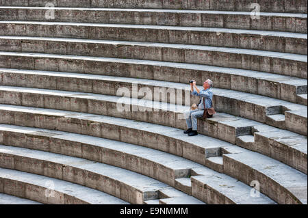 Tourist sitting on the steps of the Roman Théâtre antique d'Orange / Ancient Theater of Orange, Vaucluse, France Stock Photo