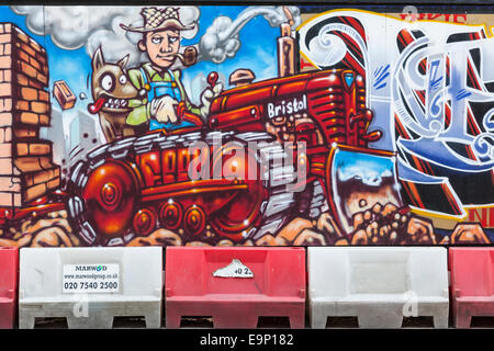 Close-up of a colourful mural featuring a man and dog riding on a tractor on temporary hoardings around a building site. Stock Photo