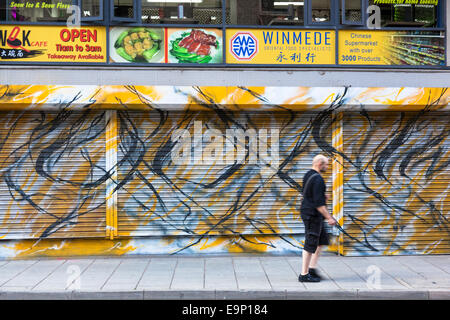 Man walks past closed shop fronts with abstract decorations on the shutters. Stock Photo