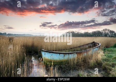 Beautiful sunset over an old rusty fishing boat washed up in reeds on the shores of Poole Harbour in Dorset Stock Photo