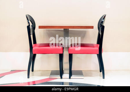 Two unoccupied red restaurant chairs by the wall Stock Photo