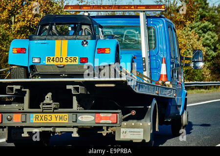 A pale blue Caterham sports car strapped onto a recovery vehicle, being driven in England, UK. Stock Photo