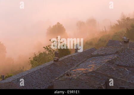Rocca Ripesena, Umbria, Italy. View over village rooftops to mist-shrouded valley, dawn. Stock Photo