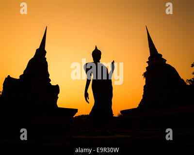 Silhouette of ancient Buddha statue and pagodas against sunset sky at Sukhothai Historical Park, Thailand. Stock Photo